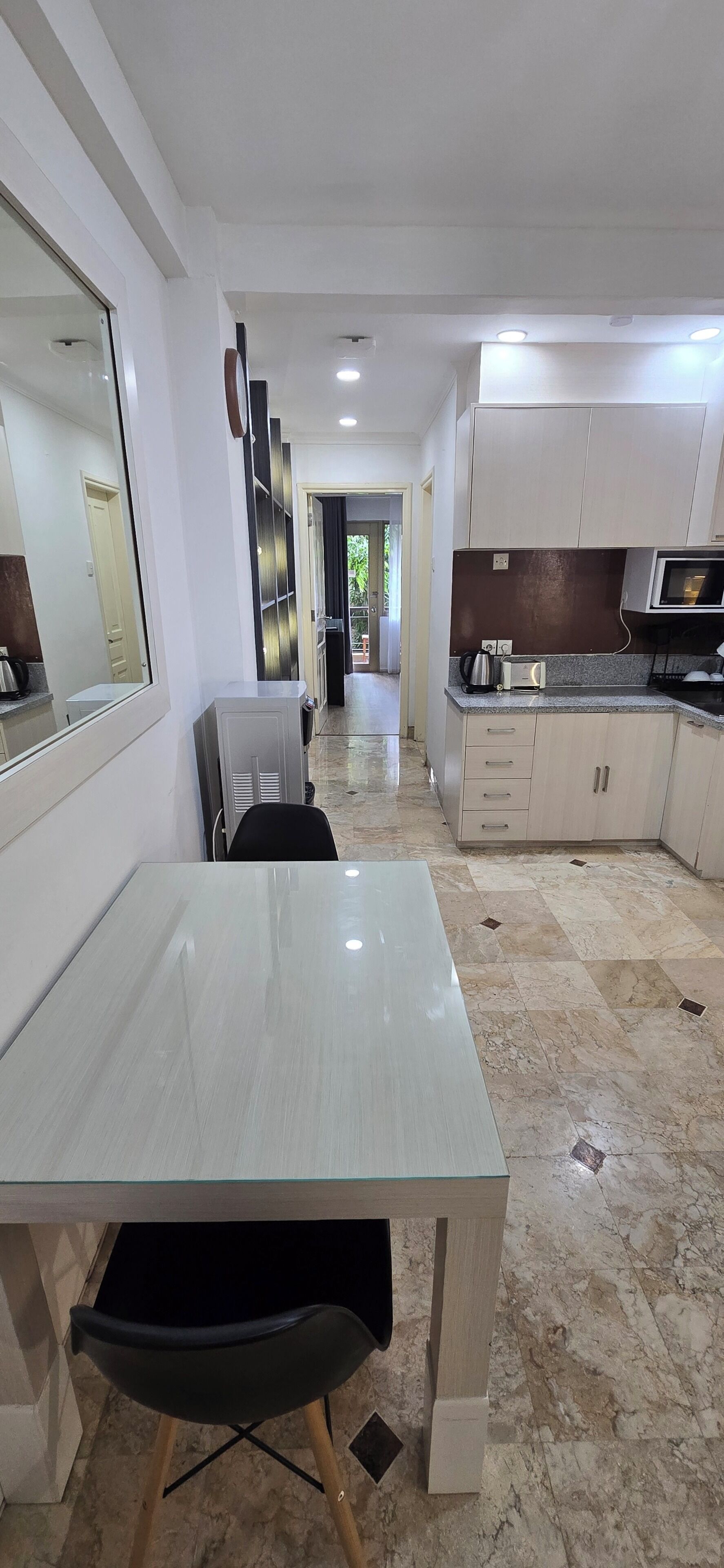 A modern kitchen with a dining area, featuring a marble floor, white cabinetry, and a large mirror.