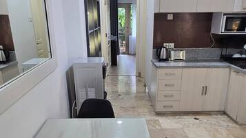 A modern kitchen with a dining area, featuring a marble floor, white cabinetry, and a large mirror.