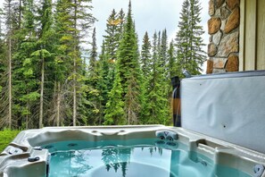 A hot tub with a stone wall and forest view. - Cozy Alpine Condo w/Hot Tub! (Sun Peaks)