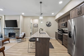 A modern kitchen with a central island, stainless steel appliances, and a stone fireplace.