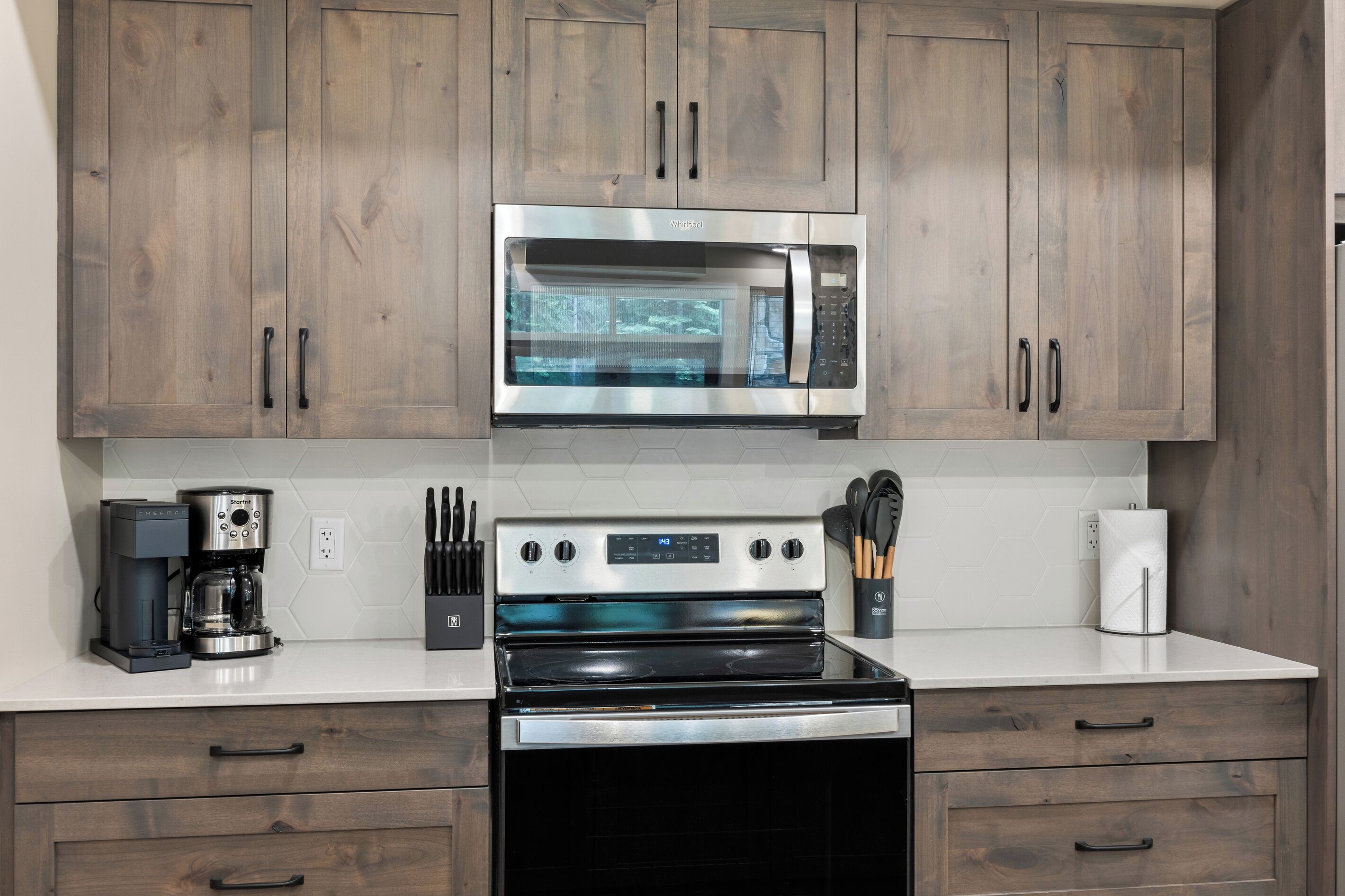 A kitchen with wooden cabinets, a stainless steel microwave, a coffee maker, and a stove.
