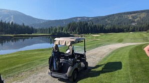 A golf cart parked on a dirt path beside a lake with a forested mountain in the background. - Cozy Alpine Condo w/Hot Tub! (Sun Peaks)