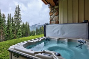 Ein Whirlpool vor einer Wand aus Stein, umgeben von Wald und Blick auf die Berge.