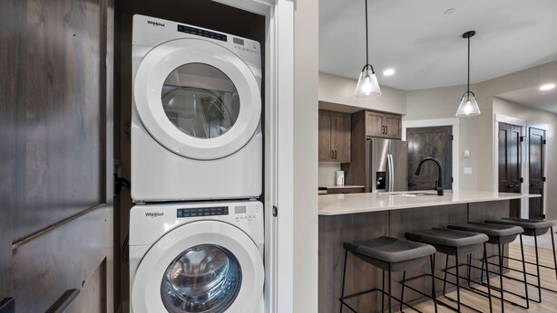 A modern kitchen with a stacked washer and dryer, bar stools, and pendant lighting. - Cozy Alpine Condo w/Hot Tub! (Sun Peaks)