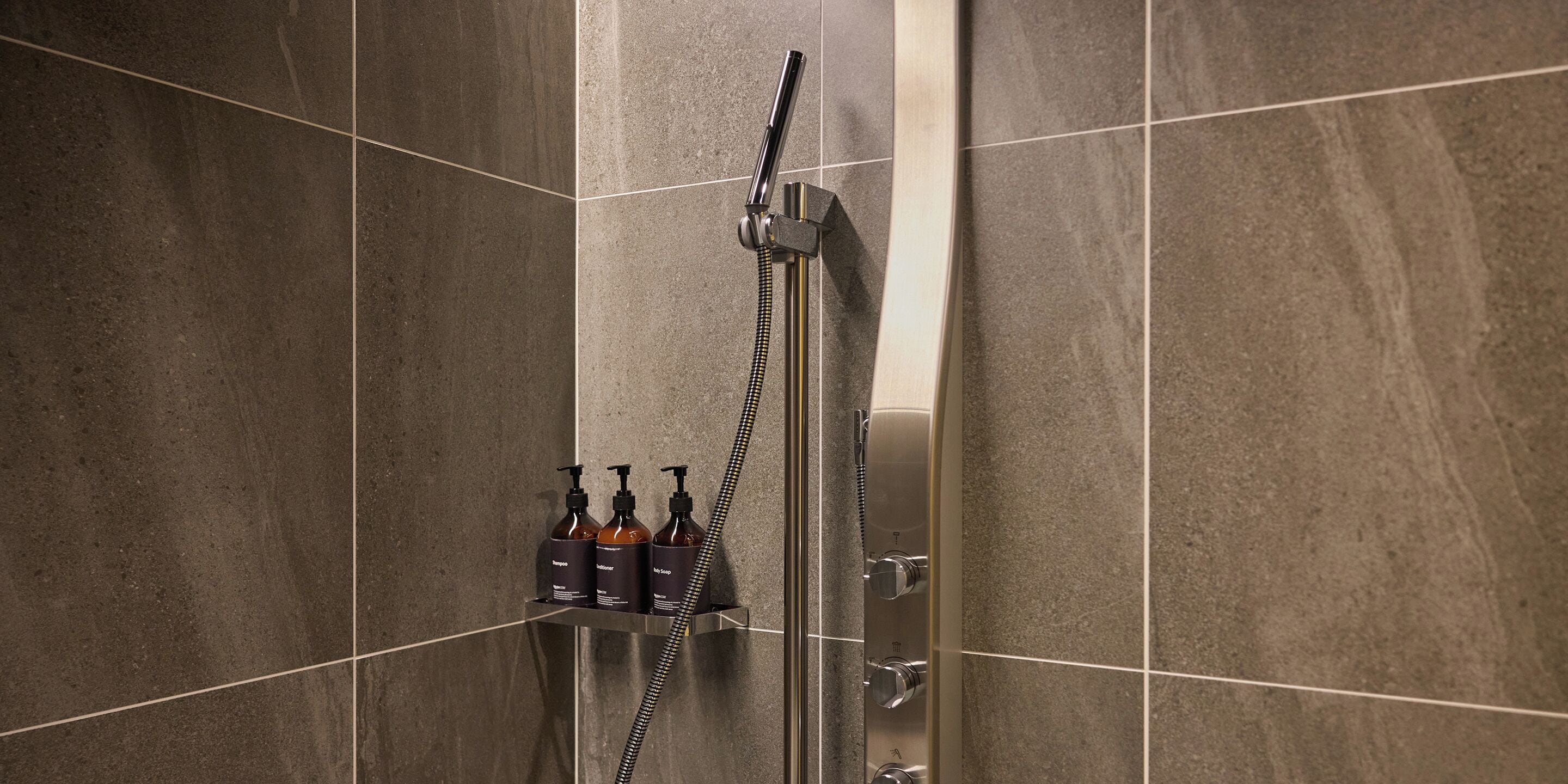 A shower with a handheld showerhead and a wall-mounted control panel.
