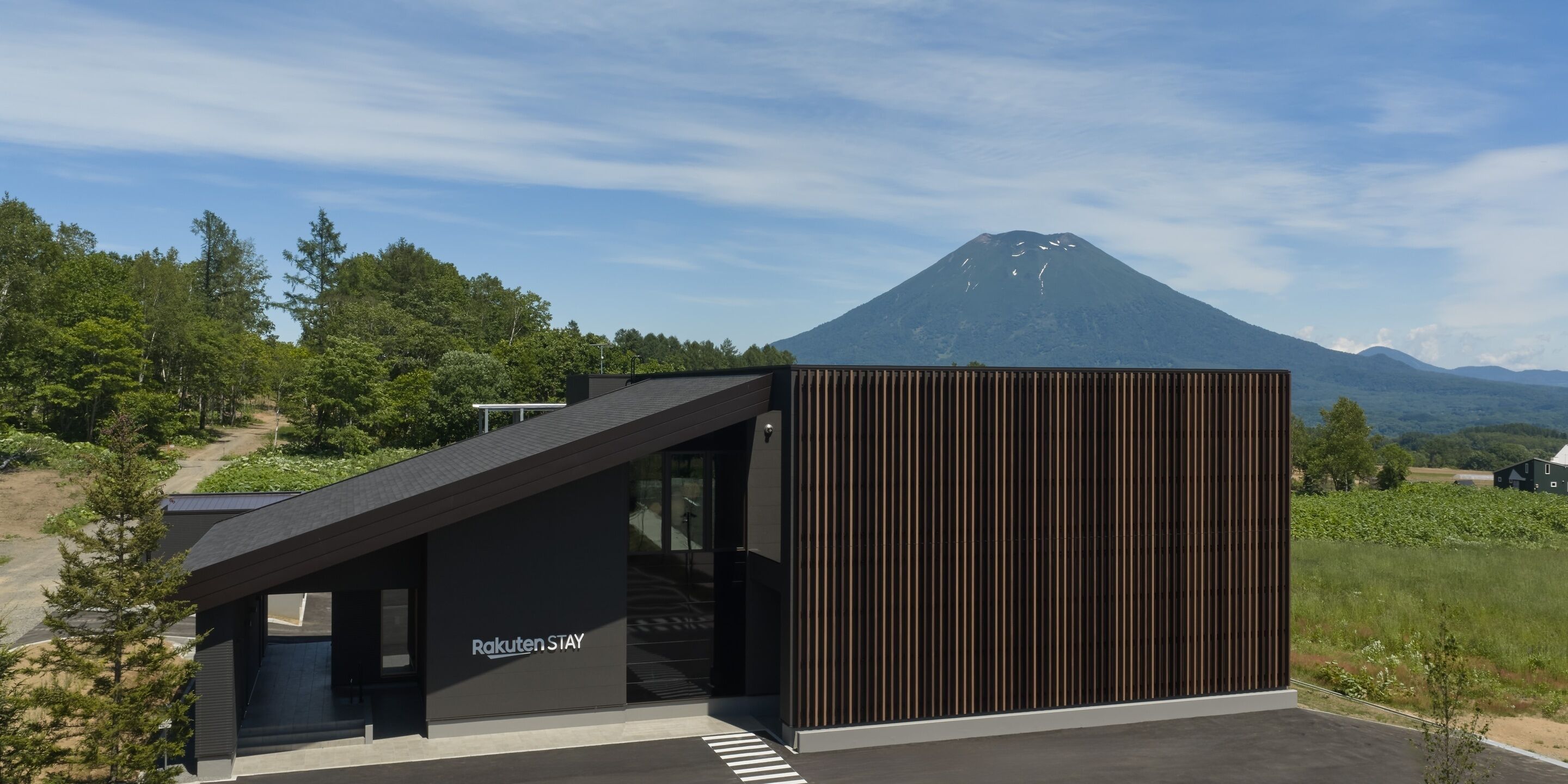Un edificio moderno con techo inclinado y una placa con la leyenda 'Rakuten STAY'.