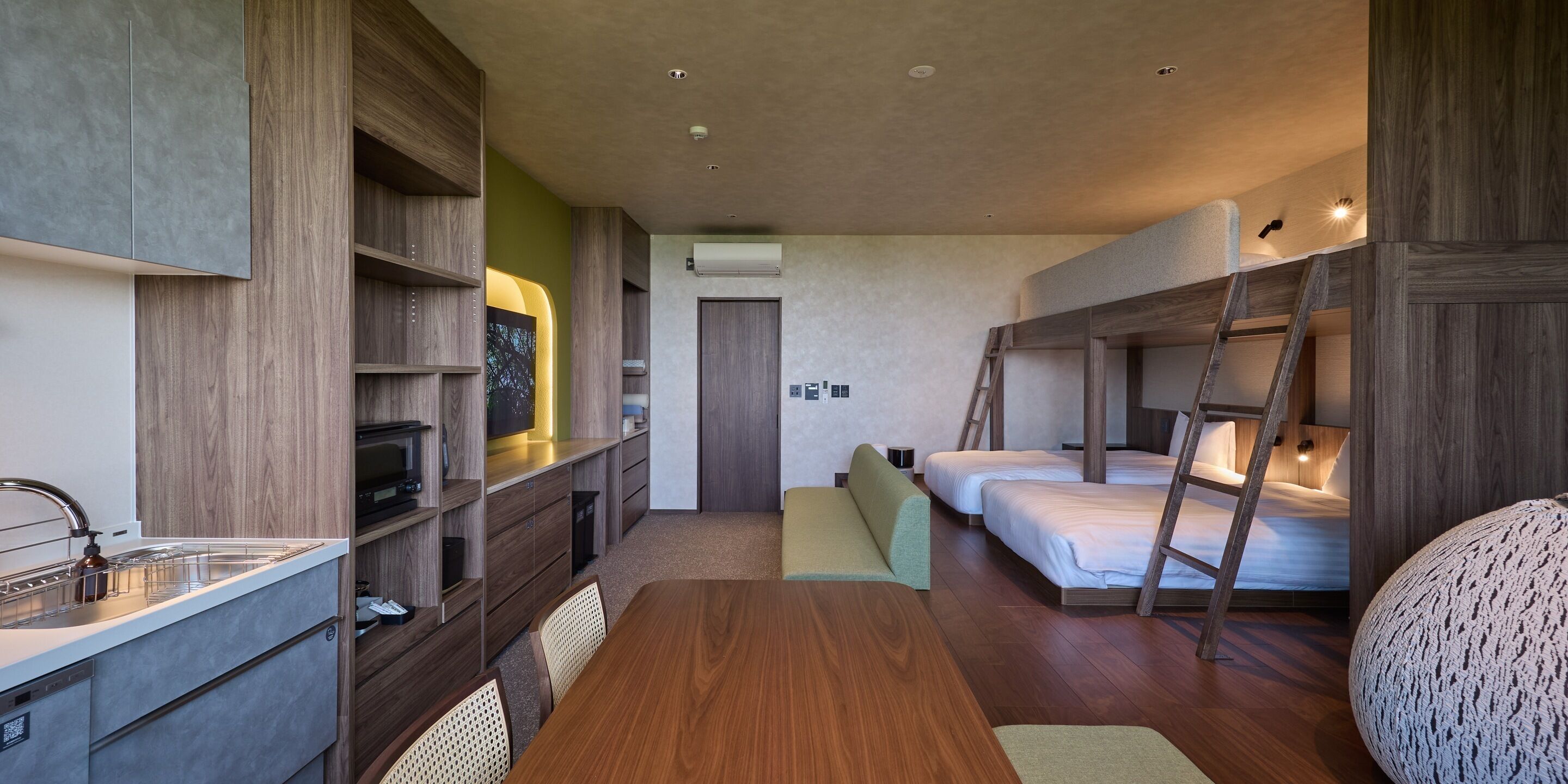 A compact hotel room with a kitchenette, a dining area, and a bunk bed.