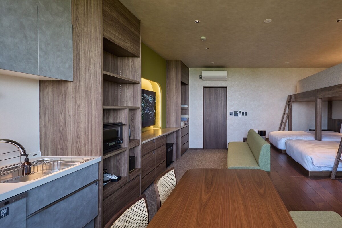 A compact hotel room with a kitchenette, a dining area, and a bunk bed.