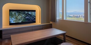 Una habitación moderna con una televisión de pantalla plana montada en la pared, un banco de madera y una ventana con vistas a casas y montañas.