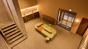 En hotellobby med en receptionsdisk, et siddeområde med sofa og skammel, og en trappe til de øvrige etager.