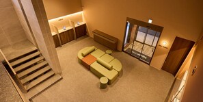 A hotel lobby with a check-in counter, a seating area with a sofa and ottoman, and a staircase leading to other floors.