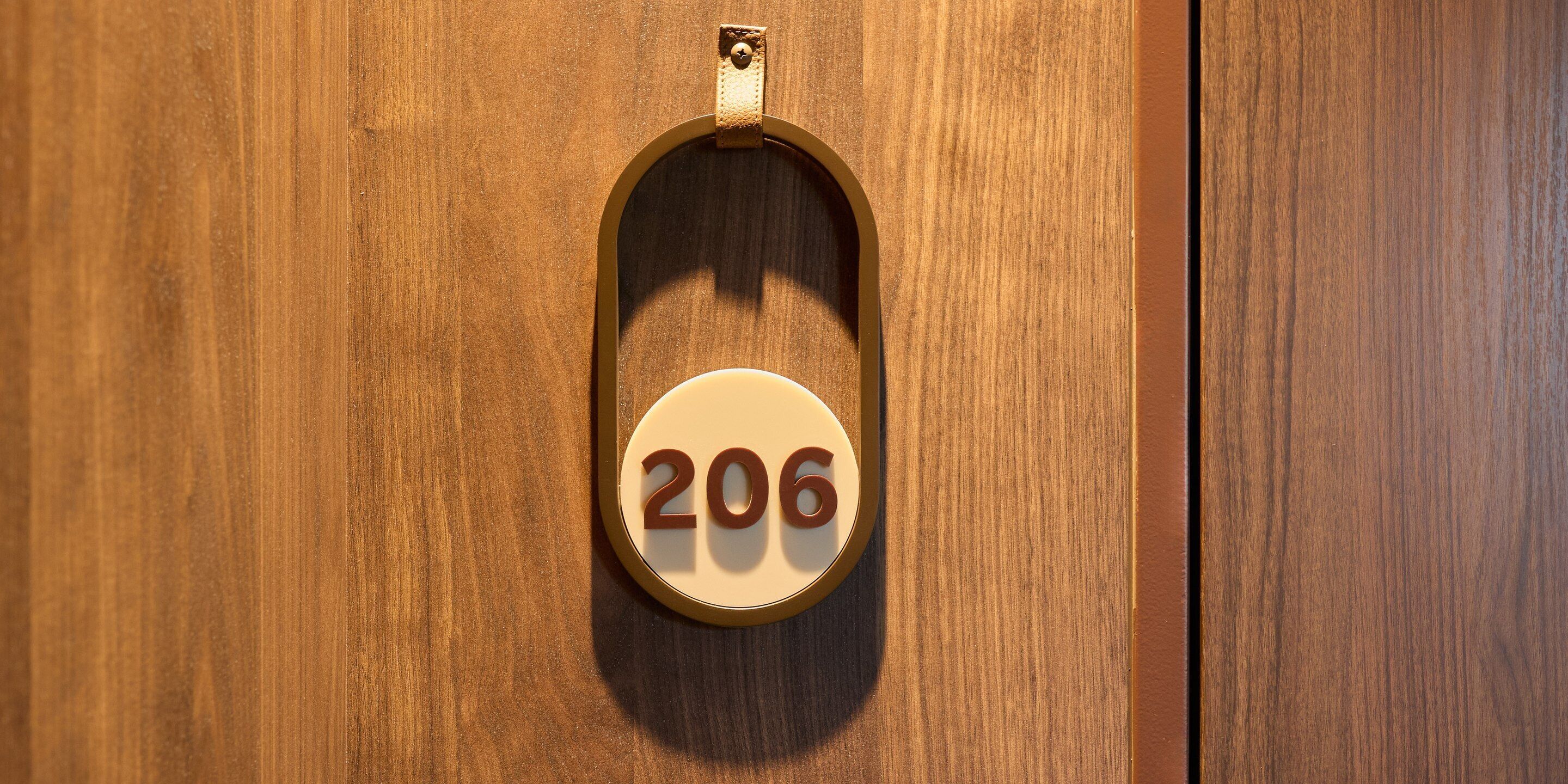 A wooden door with a brass doorbell and a white circular plaque with the number '206'.