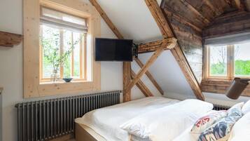 A bedroom with a sloped ceiling, a bed, a window, a radiator, and a mounted television.