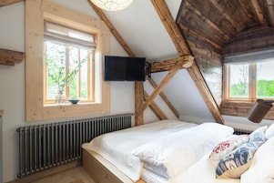 A bedroom with a sloped ceiling, a bed, a window, a radiator, and a mounted television.