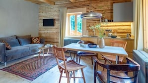 Ein gemütliches Blockhaus-Interieur mit Holzbalkendecke, einer Essecke mit Tisch und Stühlen, einer Couch und einer Küchenzeile.