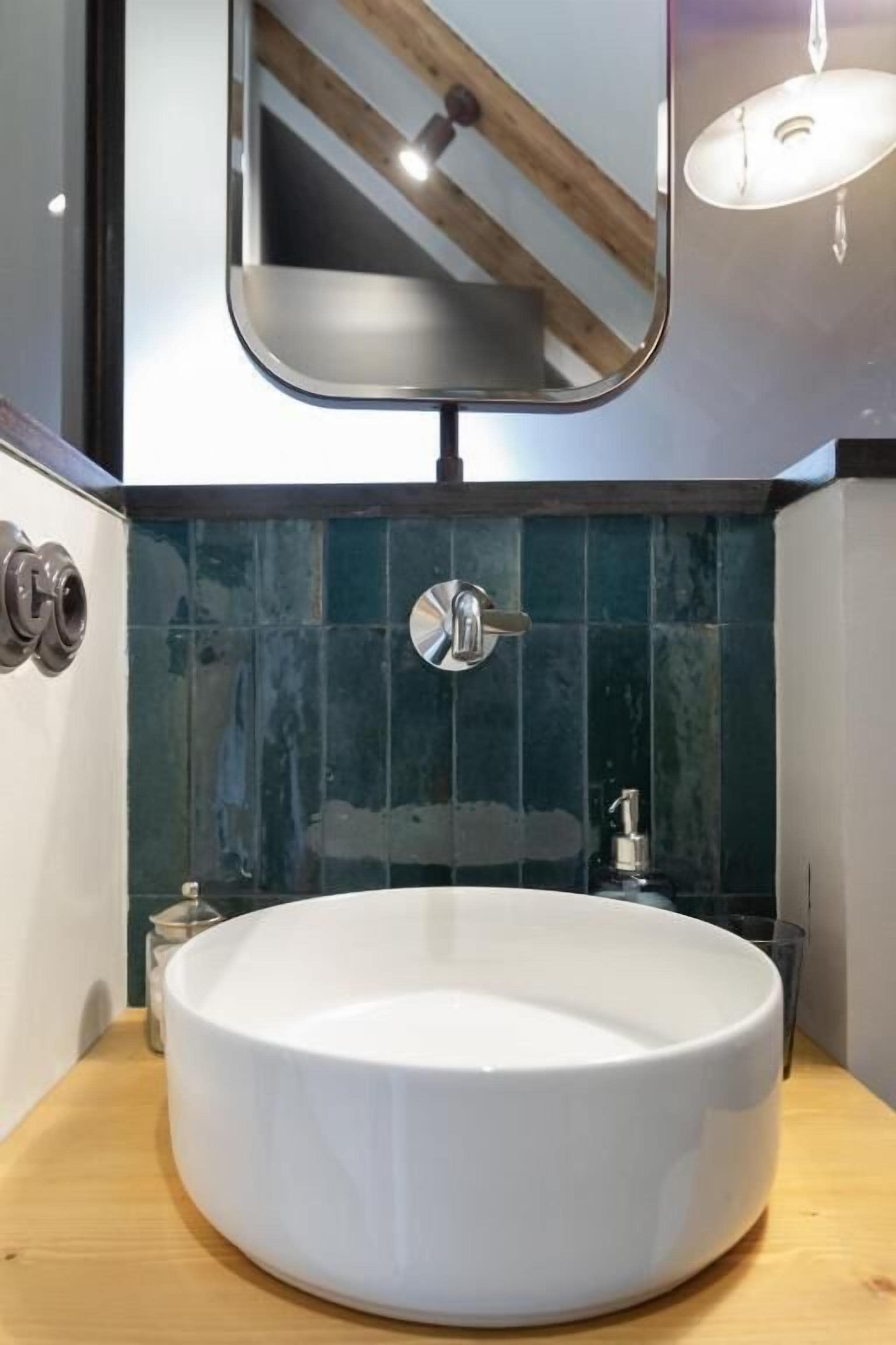 Une salle de bain moderne avec un lavabo rond blanc, un miroir et un plan de travail en bois.