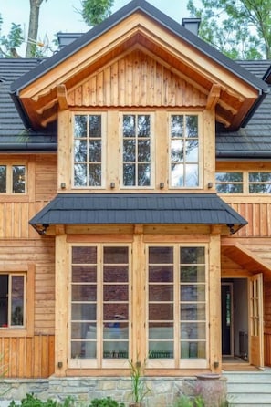 A two-story wooden house with a gabled roof and large windows.