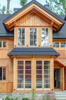 A two-story wooden house with a gabled roof and large windows.