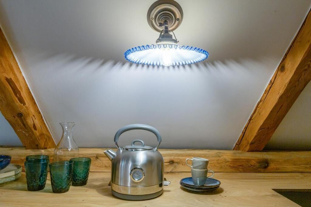 A room with a wooden ceiling, a kettle, a cup, and glasses on a table.