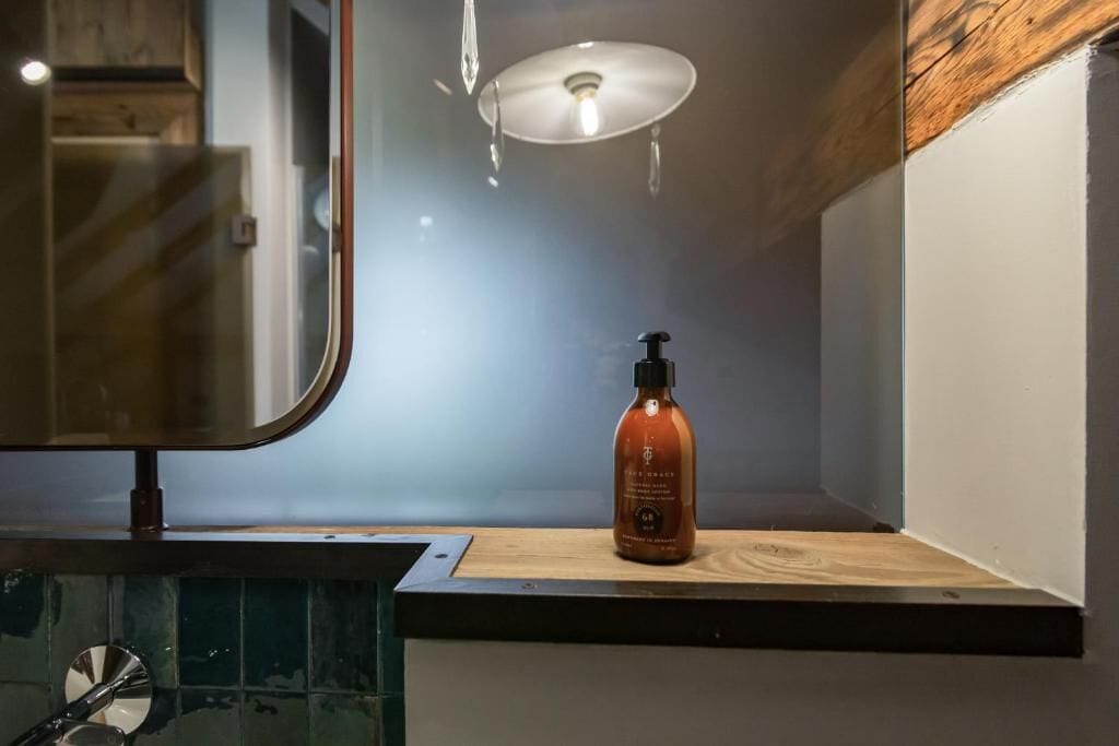 A bathroom with a wooden vanity, a mirror, and a bottle of soap on the counter.