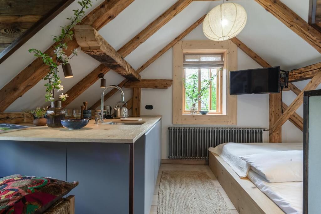A cozy attic bedroom with a sloped ceiling, a wooden bed, a small window, and a TV mounted on the wall.