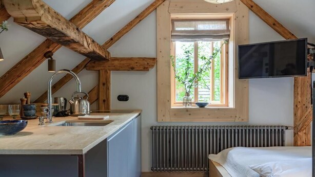 Eine kompakte Küche mit Holzboden, einem Fenster mit Blick auf Grünflächen, einem integrierten Fernseher und einer Heizung.
