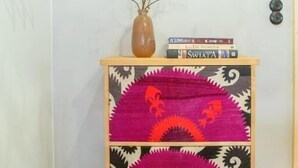 Ein Holzkabinett mit bunter Stoffbezug, eine Vase mit Zweigen und einige Bücher darauf.