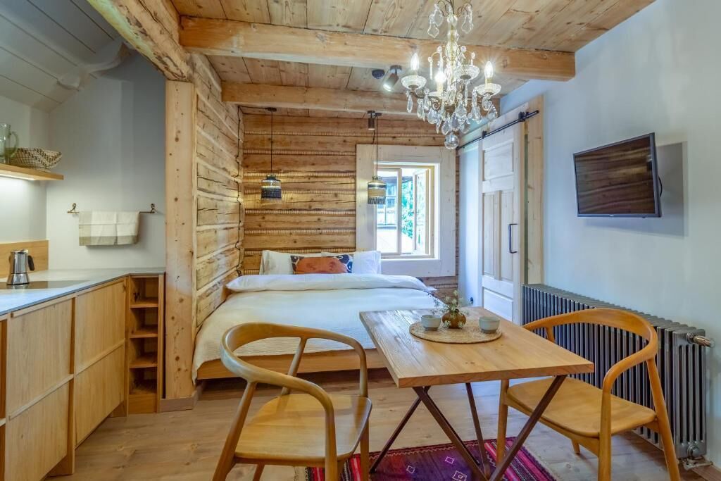 Une pièce chaleureuse avec un plafond en bois, un lit avec des oreillers, une table avec des chaises, un lustre et un téléviseur fixé au mur.