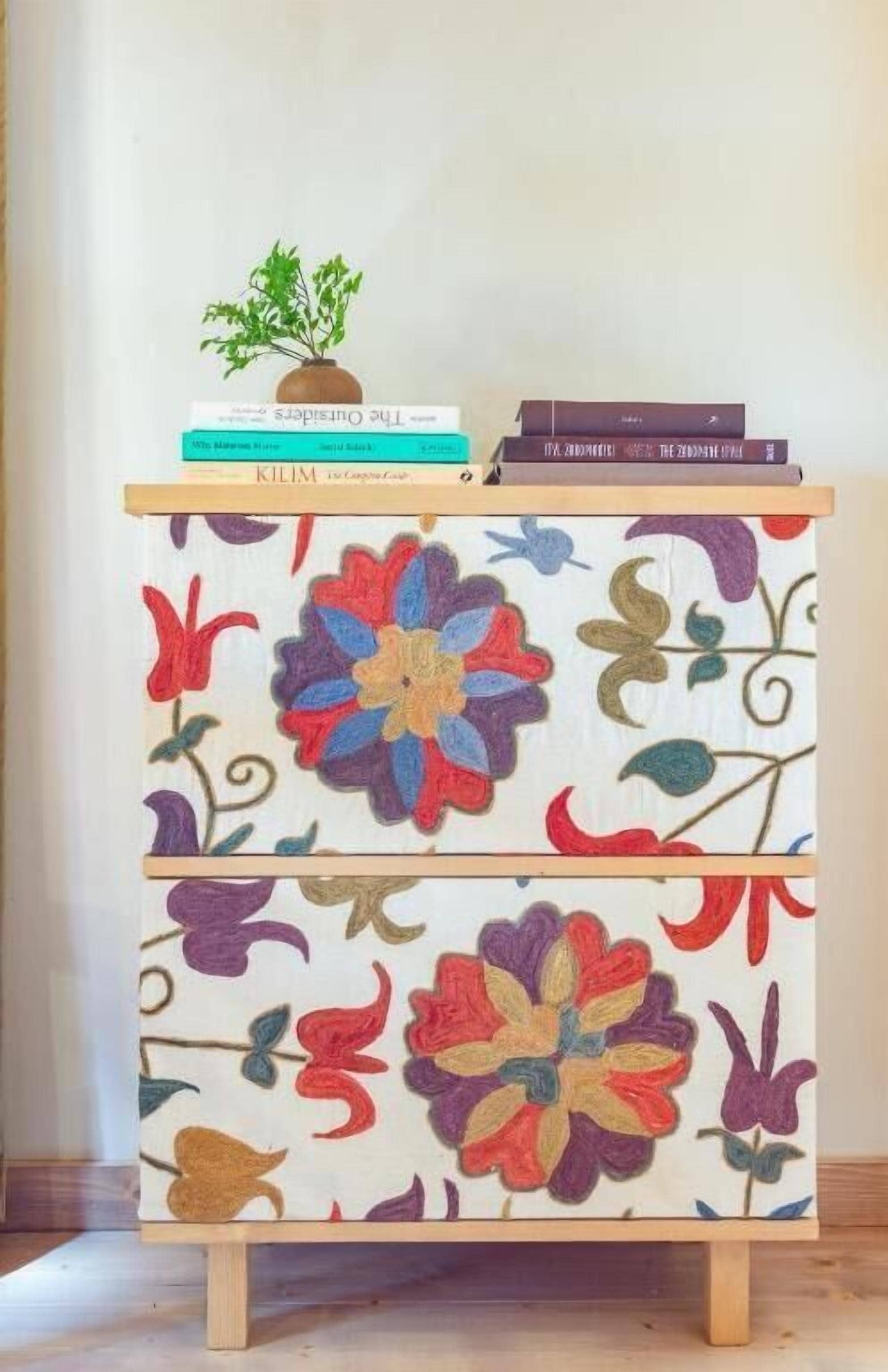 Un meuble en bois recouvert d’un tissu à motifs floraux, une petite plante et une pile de livres.