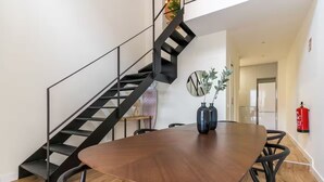 A dining area with a round table, black metal staircase, and a fire extinguisher on the wall. - Edmond Vibes Plaza de Castilla (Madrid)
