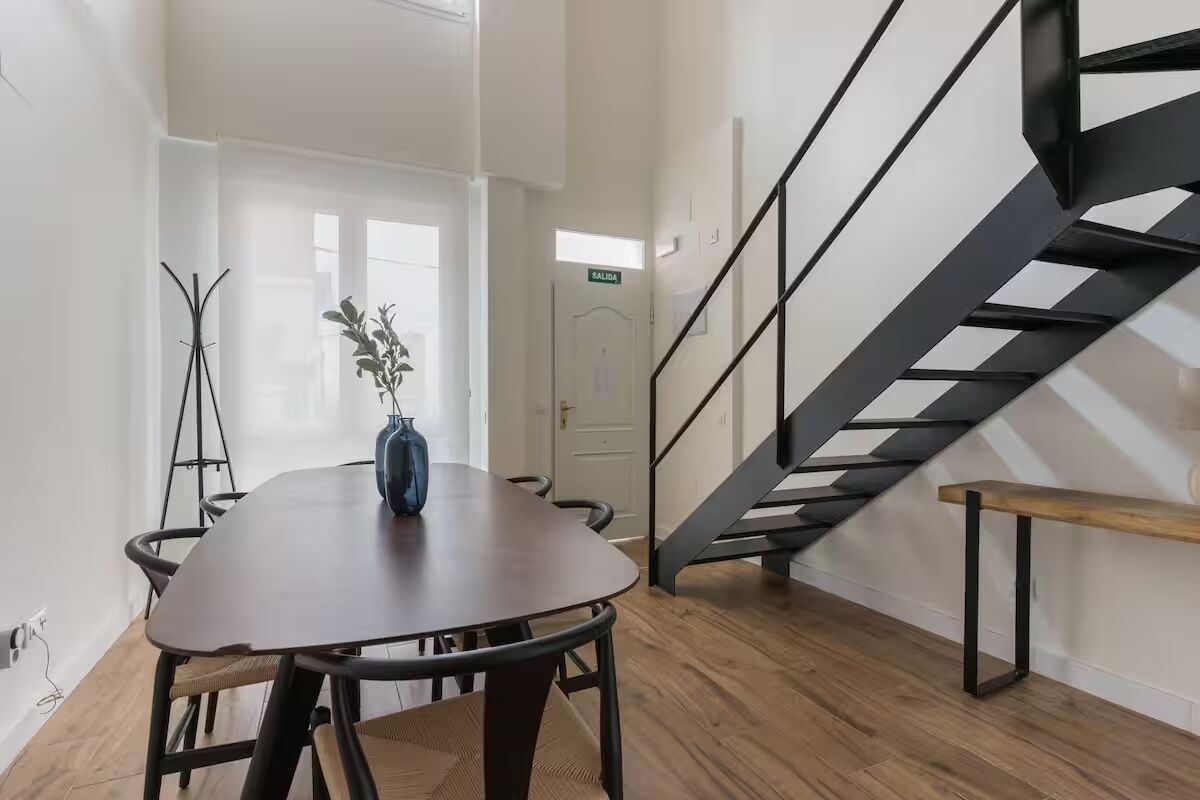 Un intérieur moderne avec une table à manger en bois, un banc et un escalier doté d’une rampe en métal.