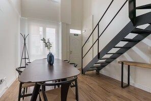 Un interior moderno con una mesa de comedor de madera, un banco y una escalera con barandilla de metal.