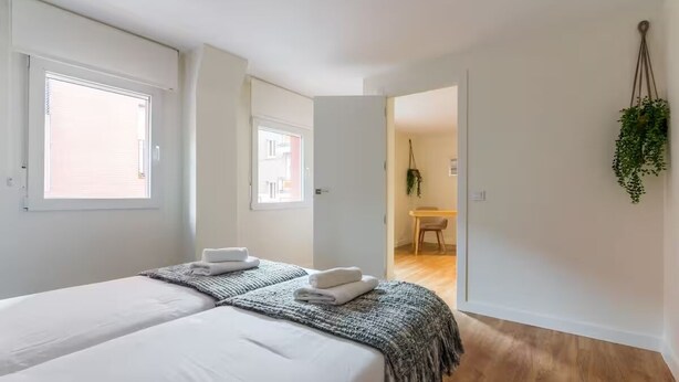 A bedroom with two beds, a wooden floor, and a view of a dining area through an open door. - Edmond Vibes Plaza de Castilla (Madrid)