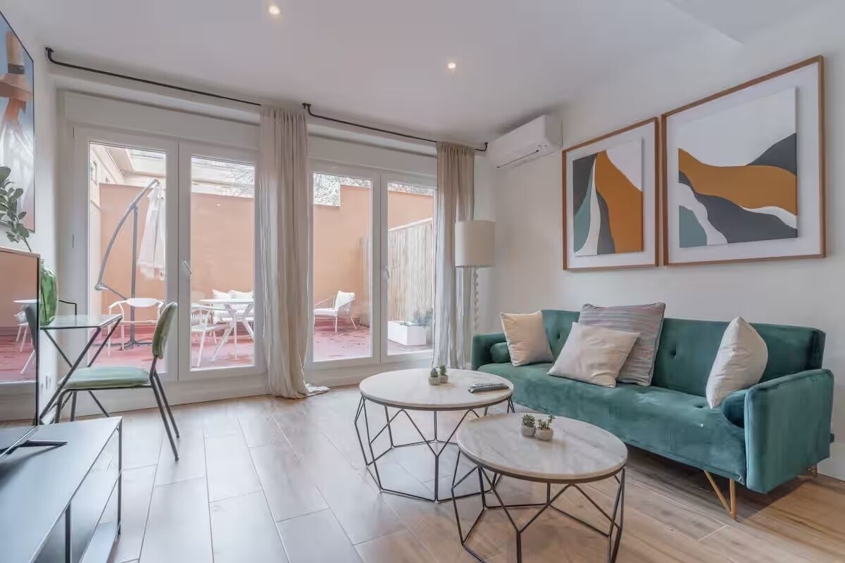 Un salon moderne avec un canapé vert, deux tables rondes et une porte en verre donnant sur un espace extérieur.