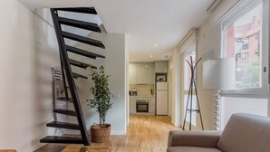 A modern living room with a staircase, a sofa, a coffee table, and a view into the kitchen. - Edmond Vibes Plaza de Castilla (Madrid)
