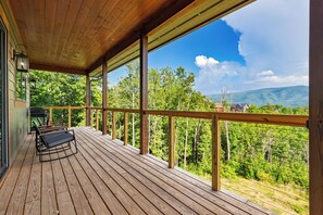 Eine Holzterrasse mit Geländer, einer Bank und Blick auf Wald und Berge.