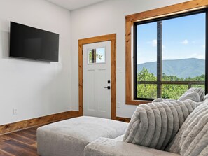 Una habitación con un ventanal grande, televisor de pantalla plana y piso de madera.