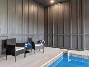 Ein Poolbereich mit zwei Korbstühlen, einem Tisch mit Flaschen und einem Pool mit weißem Rand.