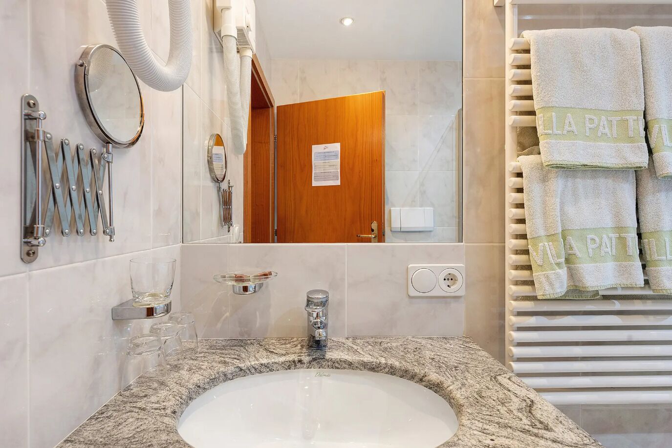 A bathroom with a sink, mirror, towel rack, and a door leading to another room.