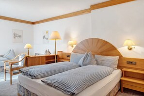 A hotel room with a bed, two bedside tables, a desk, a chair, and two wall-mounted lamps.