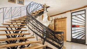 A spiral staircase with wooden steps and black metal railings, leading to a chandelier. - B&B Villa Pattis (Vipiteno)