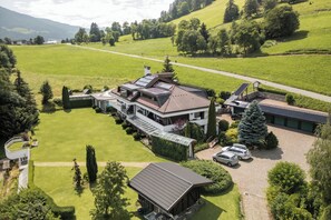 A large, modern house with multiple levels, a spacious lawn, and a driveway with parked cars.