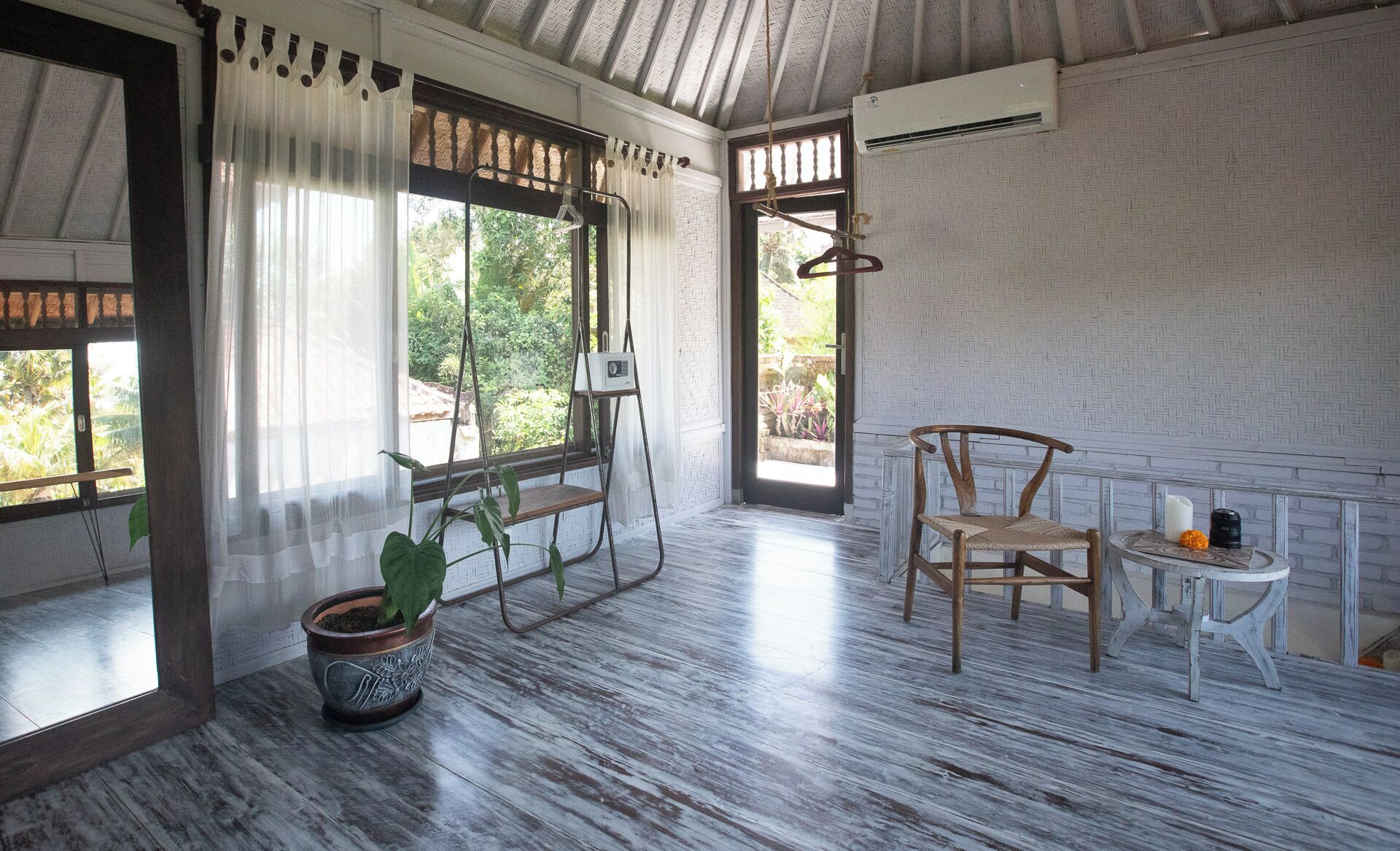 Una habitación con suelo de madera, una silla colgante, una mesita con velas y una planta en maceta.