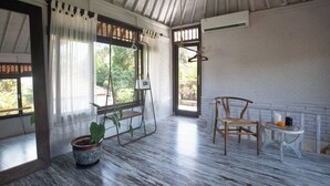 Una habitación con suelo de madera, una silla colgante, una mesita con velas y una planta en maceta.
