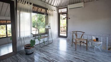 Una habitación con suelo de madera, una silla colgante, una mesita con velas y una planta en maceta.
