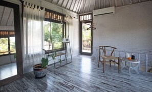 A room with a wooden floor, a hanging chair, a small table with candles, and a potted plant. - Brahma 11.11 Penestanan Ubud Apartment (Gianyar)