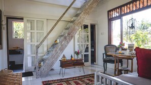 Una habitación con una escalera de madera, un comedor con mesa y sillas, un sofá rojo y vistas a zonas verdes.
