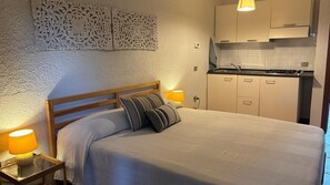 Ein Schlafzimmer mit Bett, Nachttischlampen, einem Holz-Kopfteil, einer Wandverkleidung und einer Küchenzeile mit Schränken und Herd.
