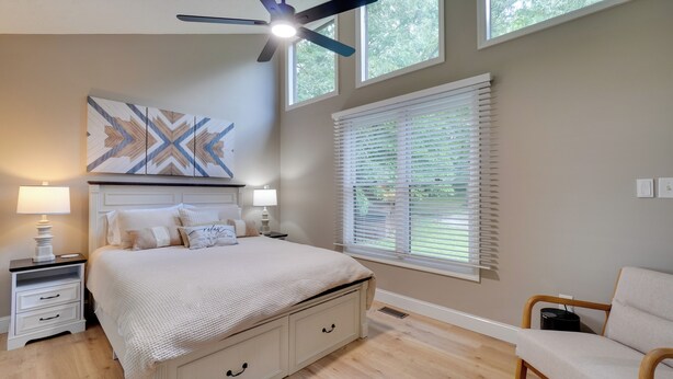 Quarto com cama, mesas de cabeceira, ventilador de teto, janela com persianas e uma cadeira.