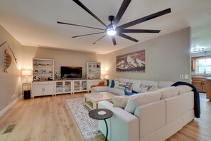 Un salon moderne avec un canapé blanc, un téléviseur à écran plat et un ventilateur de plafond.